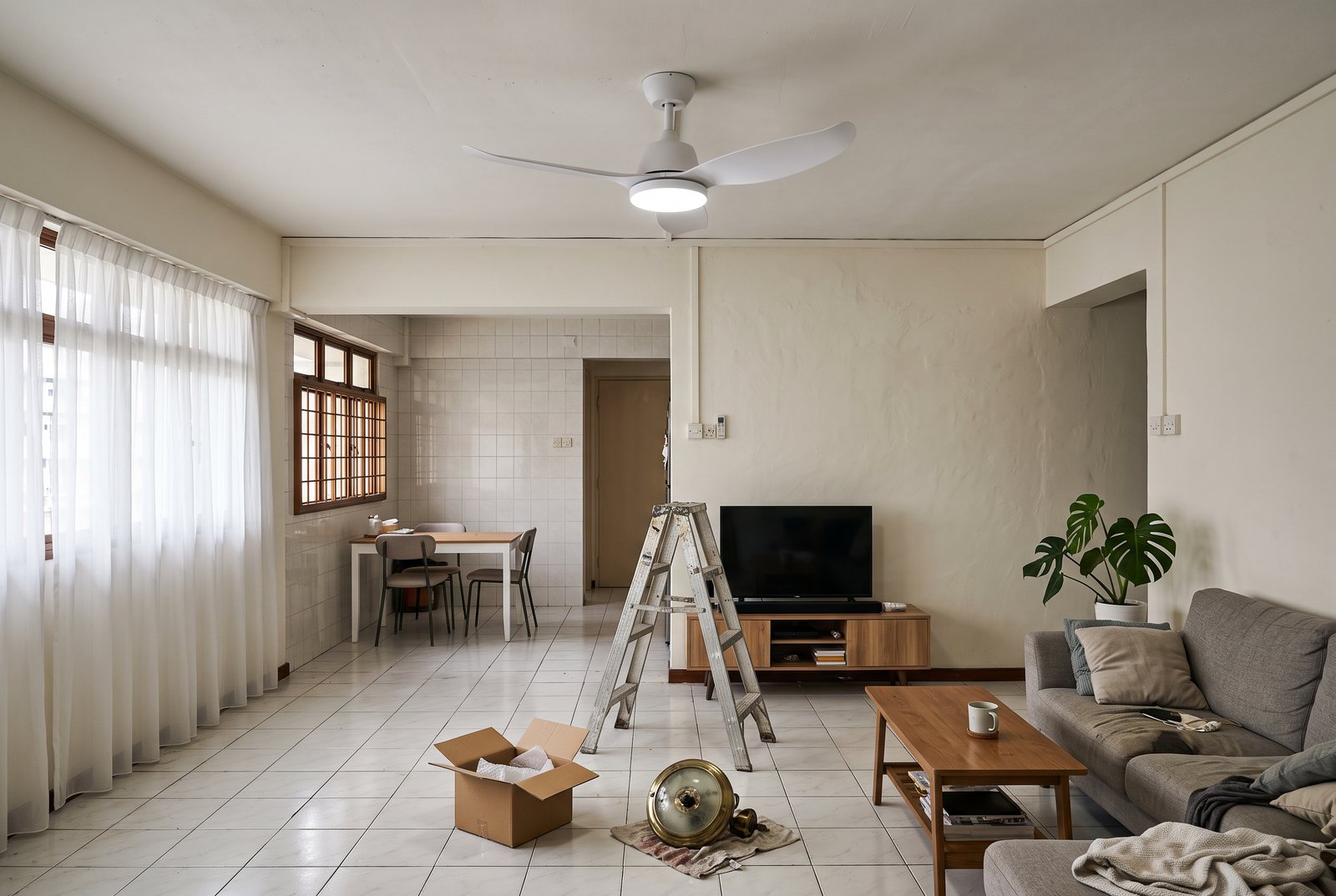 A new white three-blade ceiling fan with an LED light installed in an HDB flat living room, with the ladder and the old light fitting still on the floor